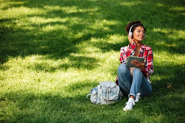 Glückliche junge Afrikanerin sitzt draußen im Park. — Stockfoto