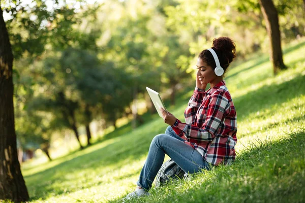 Glückliche junge Afrikanerin sitzt draußen im Park. — Stockfoto