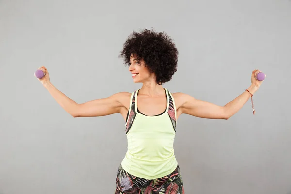 Smiling woman doing exercise with dumbbells and showing her biceps — Stock Photo, Image