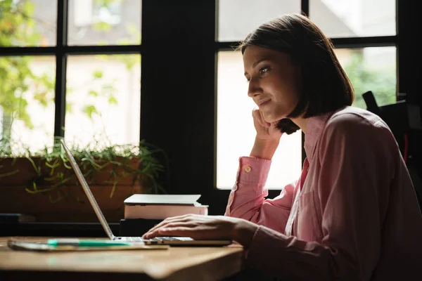 Vista lateral de la mujer sonriente sentada junto a la mesa en la cafetería — Foto de Stock