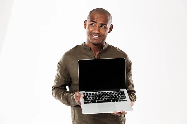 Sorrindo homem africano pensativo mostrando tela de computador portátil em branco — Fotografia de Stock