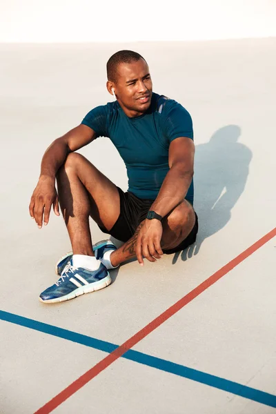 Retrato de un atleta africano sonriente en auriculares descansando — Foto de Stock