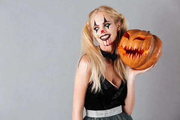 Sorridente donna bionda in Halloween make-up in posa con zucca intagliata — Foto Stock