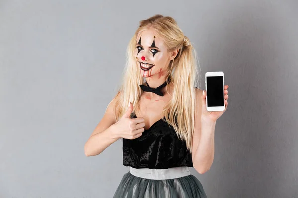 Mosolygó, szőke nő halloween alkotja a bemutatás smartphone — Stock Fotó