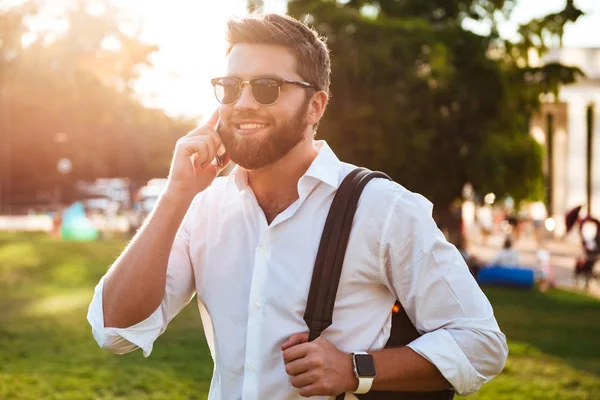Happy bearded man in sunglasses standing outdoors while holding backpack — Stock Photo, Image