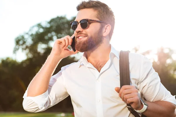 Χαμογελώντας όμορφος γενειοφόρος άνδρας με γυαλιά ηλίου που μιλάει με το smartphone — Φωτογραφία Αρχείου
