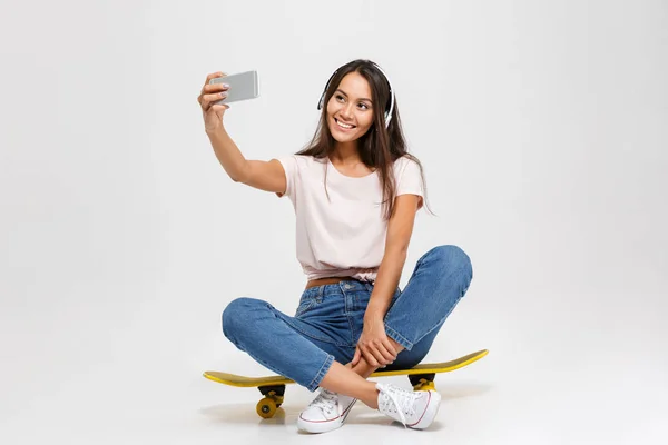 Porträtt av ung glad tjej i vita hörlurar gör selfie — Stockfoto
