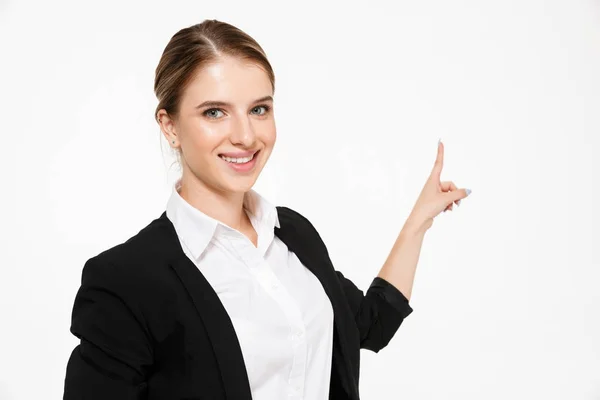 Smiling blonde business woman pointing back and looking at camera — Stock Photo, Image