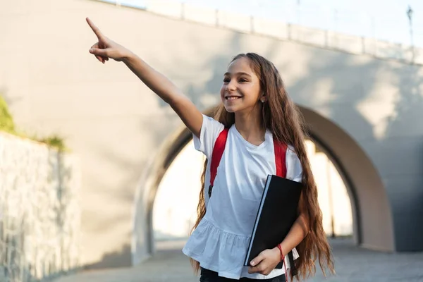 Glimlachend brunette schoolmeisje poseren buitenshuis aan te wijzen en op zoek weg — Stockfoto