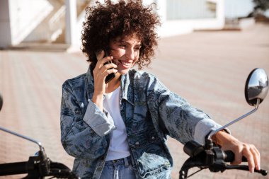 Açık havada modern motosiklet üzerinde oturan memnun kıvırcık kız