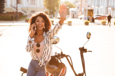 Açık havada modern motosiklet üzerinde oturan mutlu Afrika kadın