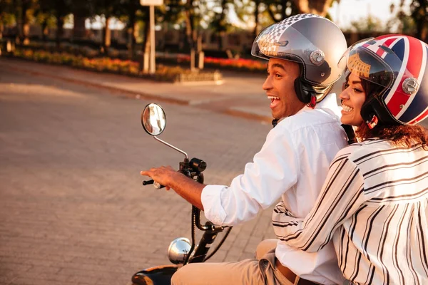 Side view of joyful african couple rides on modern motorbike