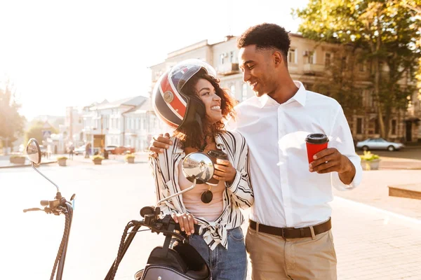 Happy young african couple drinking coffee while standing near motorbike — Stock Photo, Image