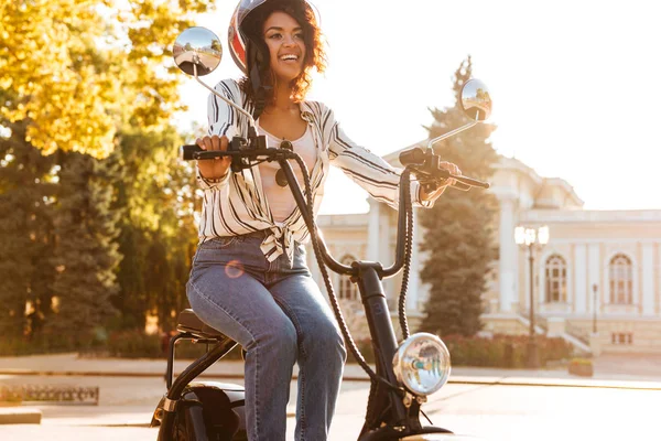 Улыбающаяся африканская женщина сидит на современном мотоцикле — стоковое фото