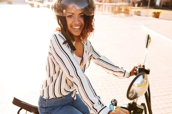 Вид сбоку улыбающейся африканской женщины, сидящей на современном мотоцикле — стоковое фото