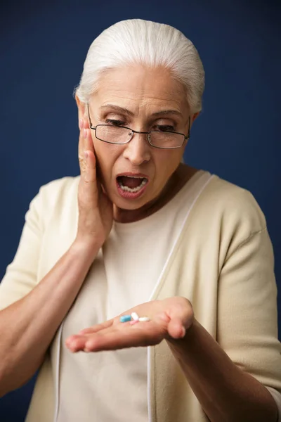 Mujer conmocionada sobre fondo azul oscuro mirando píldoras . — Foto de Stock