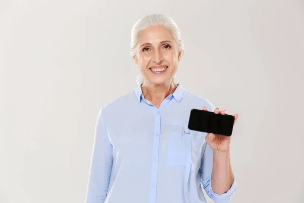 Счастливая красивая зрелая женщина показывает смартфон с чистым черным экраном изолированы — стоковое фото