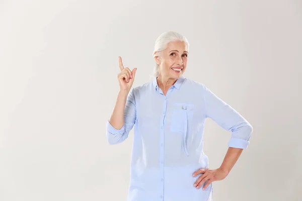 Senhora idosa alegre de cabelos grisalhos em camisa azul, apontando com finge — Fotografia de Stock