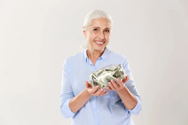 Glückliche Seniorin im blauen Hemd hält Glasbank mit Dollars in der Hand, — Stockfoto