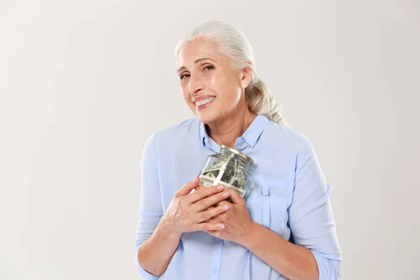 Felice donna matura sorridente abbracciando il suo vaso di vetro con dollari — Foto Stock