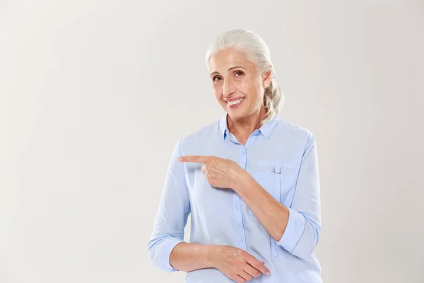 Весела стара леді в блакитній сорочці, вказуючи пальцем на емблему — стокове фото