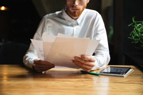 Обрезанное фото молодого бородатого человека, работающего с бумагами — стоковое фото