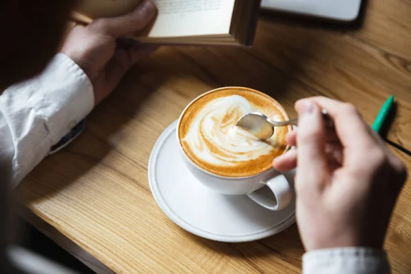 Photo recadrée de l'homme en chemise blanche brassant du café pendant la lecture — Photo