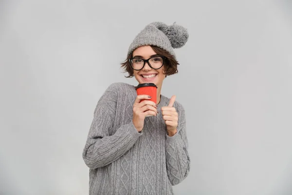 Ευτυχισμένη γυναίκα ντυμένη με πουλόβερ και ζεστό καπέλο πίνοντας καφέ. — Φωτογραφία Αρχείου