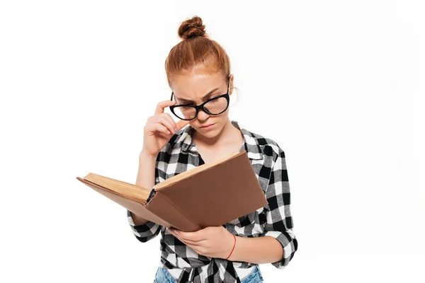 Концентрированная рыжая женщина в очках, читающая книгу — стоковое фото