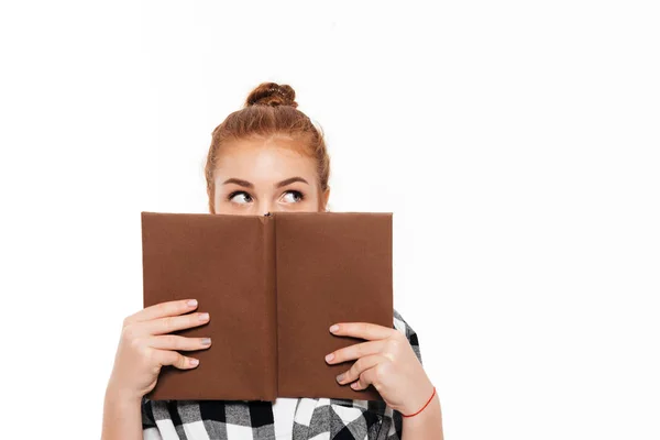 Ung ingefærkvinne i skjorte som gjemmer seg bak en bok – stockfoto