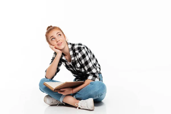 Pensive ginger woman in shirt sitting on floor with book — Stock Photo, Image
