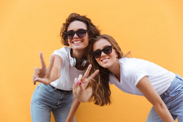 Two happy cheerful teenage girls in sunglasses showing peace gesture — Stock Photo, Image
