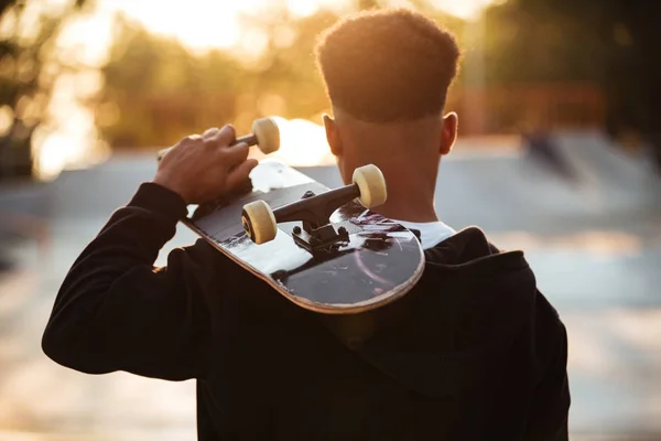 Achteraanzicht van een mannelijke tiener jongen holding skateboard — Stockfoto
