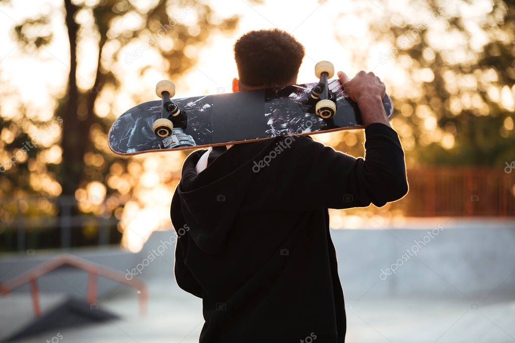 Back view of a male teenager guy holding skateboard
