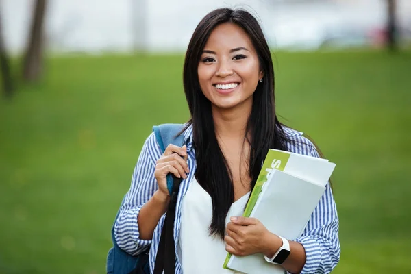 笑みを浮かべてアジア学生を持つ若い女性のバックパック、noteboo を保持 — ストック写真