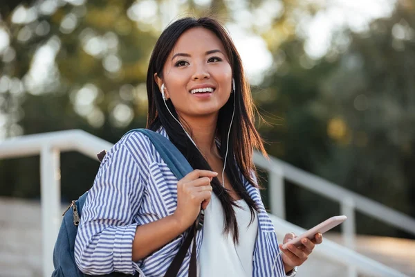 Pretty asian woman listening to music with earphones, holding mo — Stock Photo, Image