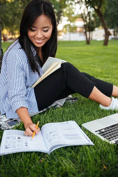 Glücklich asiatische Studentin in gestreiftem Hemd Schreiben zu Notizbuch, — Stockfoto