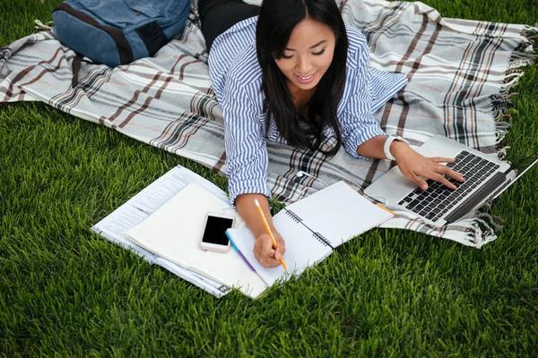 Draufsicht auf eine hübsche asiatische Studentin, die Aufzeichnungen in Papiernotizen führt — Stockfoto