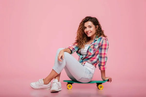 Jeune femme souriante assise sur un skateboard isolé — Photo
