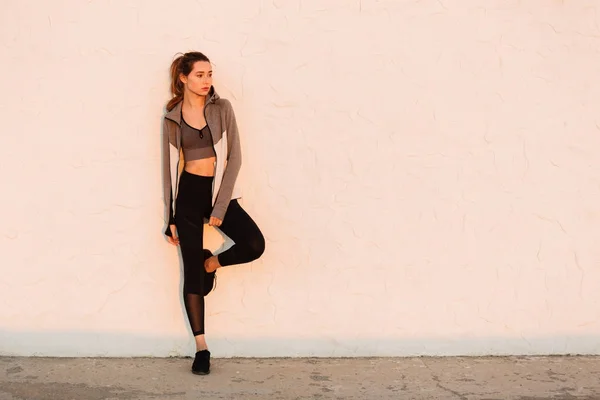 Joven hermosa mujer deportiva descansando después de correr cerca de blanco wal —  Fotos de Stock