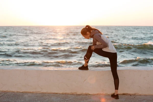 海辺で靴紐を結ぶ若いスリムなスポーツ女の写真 — ストック写真