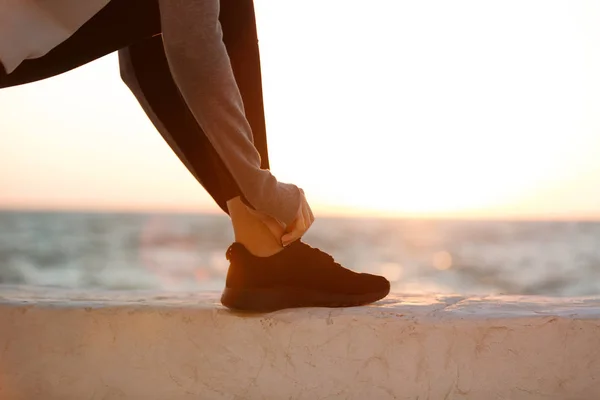 Foto ritagliata di donna sportiva allacciatura lacci di scarpe al mare — Foto Stock