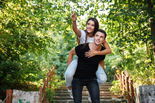 Jovem casal feliz desfrutando de passeio de piggyback no parque — Fotografia de Stock