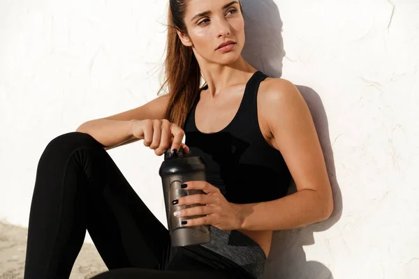 Geconcentreerd fitness dame zittend buiten drinkwater. — Stockfoto