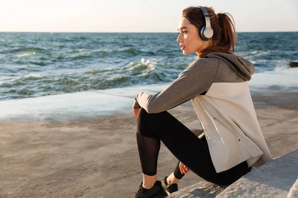 Photo de charmante femme sportive écoutant de la musique, assise sur le — Photo