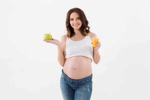 Mujer embarazada alegre bebiendo jugo sosteniendo manzana — Foto de Stock