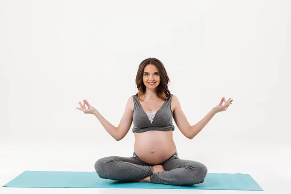 Smiling pregnant woman sitting on fitness mat and meditation — Stock Photo, Image