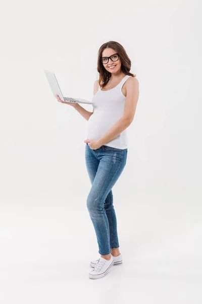 Mujer embarazada feliz usando gafas usando portátil — Foto de Stock