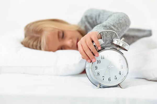 Nahaufnahme eines verschlafenen kleinen Mädchens, das den Wecker in seinem Bett ausgeschaltet hat — Stockfoto