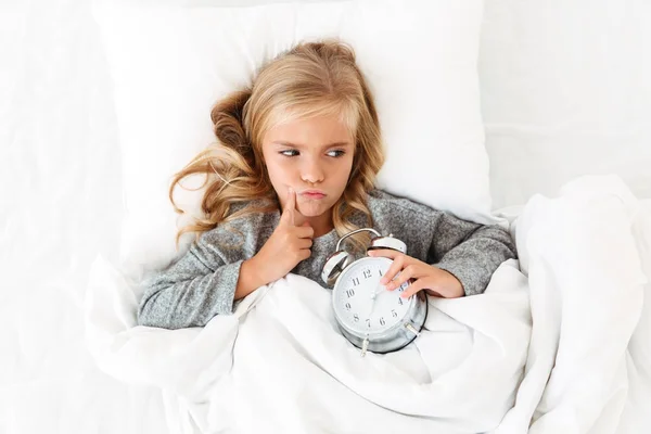 Вид сверху на маленькую девочку, лежащую в кровати с будильником — стоковое фото
